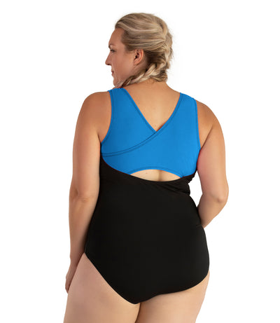 Plus size woman, back view, wearing JunoActive plus size AquaSport Crossback Tanksuit Pacific Blue Black. The crossback shoulder detail of the tanksuit is blue. The main body of the suit is solid black, keyhole opening at the mid-back.