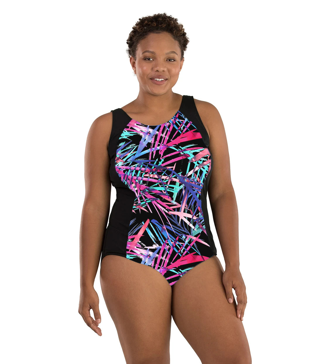 Plus size woman, facing front, wearing JunoActive plus size AquaSport Princess Seam Tanksuit Sunset Palm Print Black. Center front of suit is multi colored pink blue and black Palm print. Side panels are black, has a scoop neckline and conservative leg opening.
