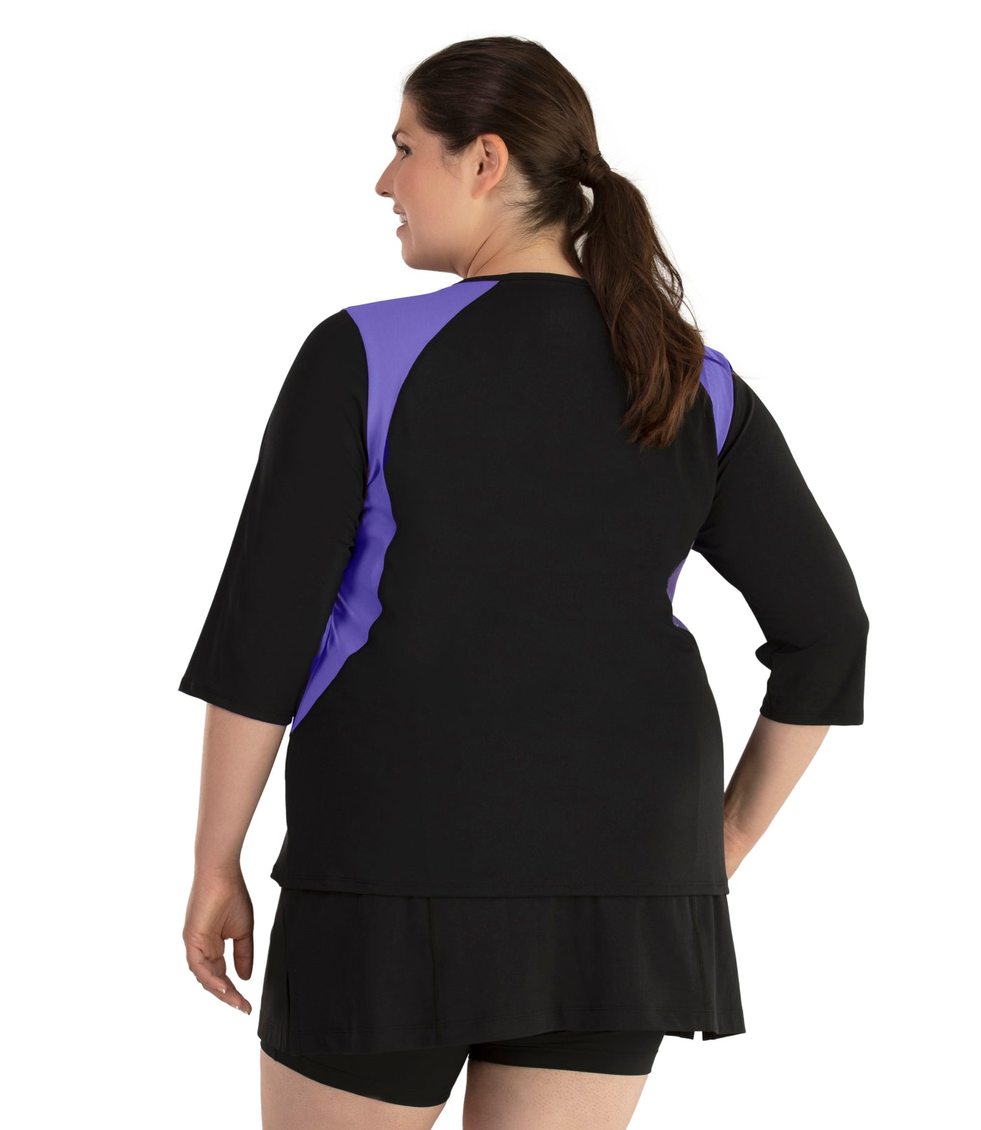 Plus size woman, facing back and side profile, wearing AquaSport Three Quarter Sleeve Rash Guard Purple and Black. V-neckline, black torso and sleeves with purple colorblock at shoulder and waist. She is wearing a pair of black JunoActive plus size swim shorts.