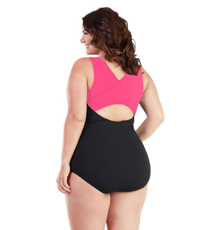 Plus size woman, back view, wearing JunoActive plus size AquaSport Crossback Tanksuit Pink Black. The crossback shoulder detail of the tanksuit is pink. The main body of the suit is solid black, keyhole opening at the mid-back.