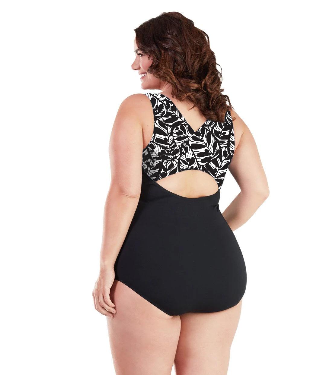 Plus size woman, back view, wearing JunoActive plus size AquaSport Crossback Tanksuit Tropical Print Black. The crossback shoulder detail of the tanksuit has a Black and white Tropical leaf print. The main body of the suit is solid black, keyhole opening at the mid-back.