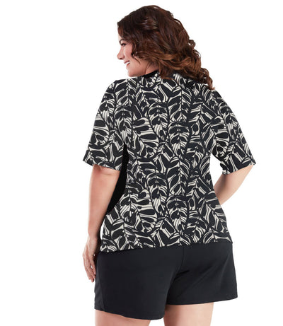 Plus size woman, back view, wearing AquaSport Colorblock Swim Tee Tropical Print. Black colorblocking on waist and shoulders. Long cover short sleeves meeting at the elbow. 