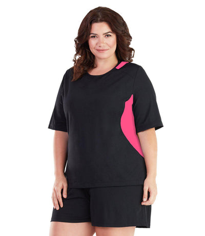 Plus size woman, facing front, wearing AquaSport Colorblock Swim Tee Pink and Black. Pink colorblocking on waist and shoulders. Long cover short sleeves meeting at the elbow and a rounded neckline. 