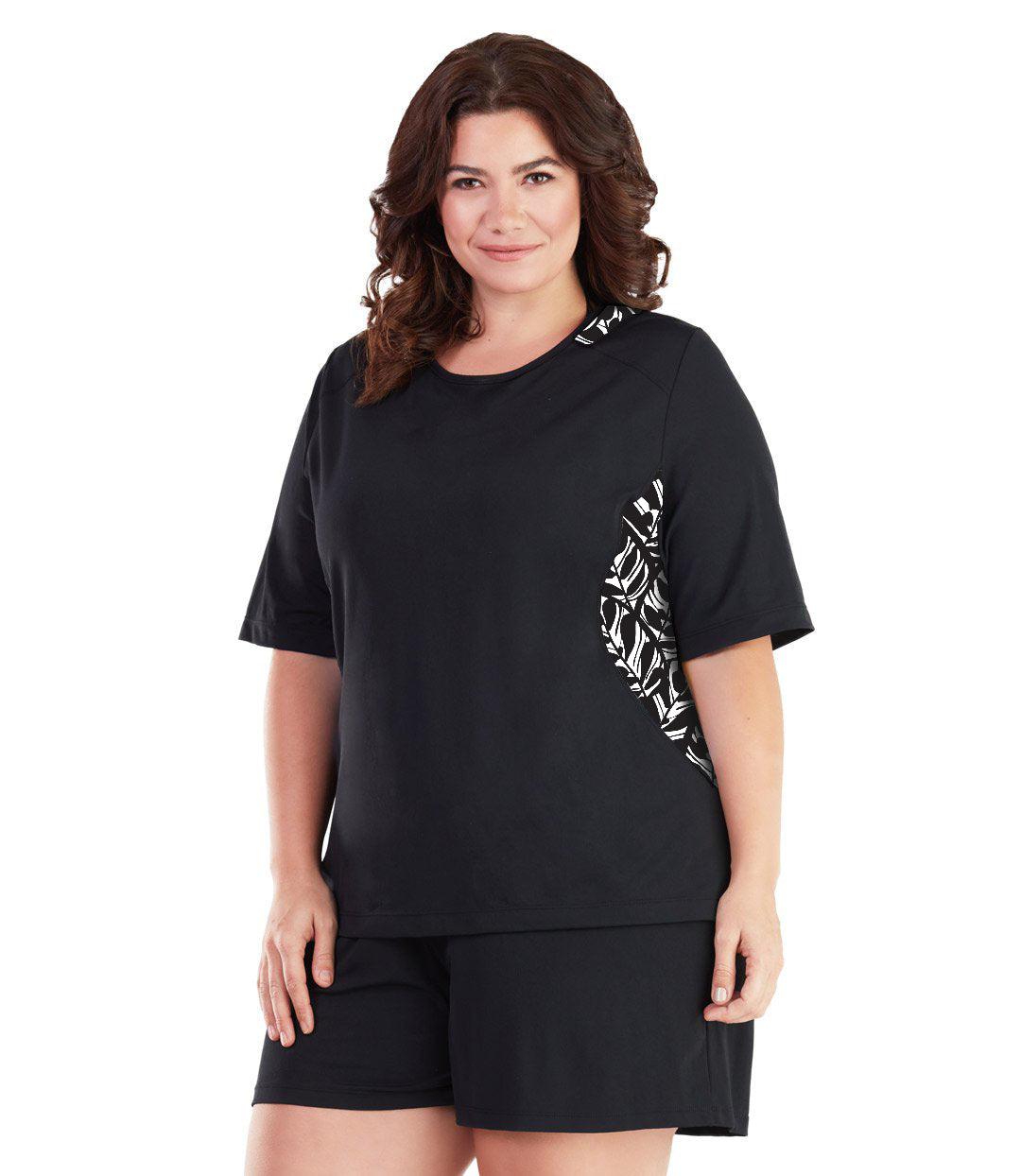 Plus size woman, facing front, wearing AquaSport Colorblock Swim Tee Tropical Black. Tropical black and white print  colorblocking on waist and shoulders. Long cover short sleeves meeting at the elbow and a rounded neckline. 