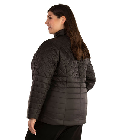 Plus size woman, back side view facing left, wearing a JunoActive plus size Quilted Active Length Jacket in black. The jacket has a mock neck collar, zip front closure, and side pockets. Jacket quilting is a diamond pattern at the shoulders and horizontal lines at the lower half of the jacket. The length of the plus size jacket hits at the hips.