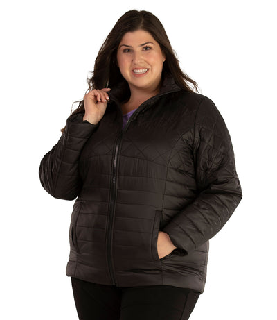 Plus size woman, front view, wearing a JunoActive plus size Quilted Active Length Jacket in black. The jacket has a mock neck collar, zip front closure and side pockets. Jacket quilting is a diamond pattern at the shoulders and horizontal lines at the lower half of the jacket. The length of the plus size jacket hits at the hips.