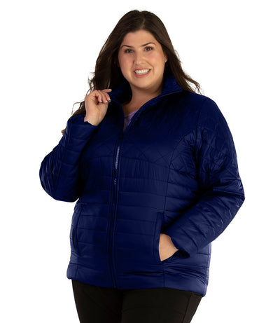 Plus size woman, front view, wearing a JunoActive plus size Quilted Active Length Jacket in Sapphire Blue. The jacket has a mock neck collar, zip front closure and side pockets. Jacket quilting is a diamond pattern at the shoulders and horizontal lines at the lower half of the jacket. The length of the plus size jacket hits at the hips.