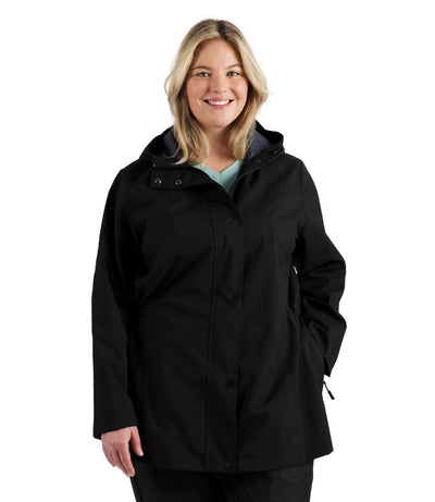 Plus size woman, front view, wearing a black JunoActive plus size wind and rain jacket. The jacket has a hood, double front closure and side pockets. The length of the plus size jacket hits just below the hips.