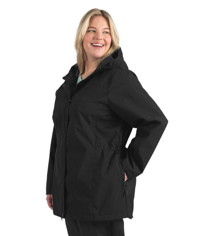 Plus size woman, side view, looking over her shoulder wearing a black JunoActive plus size wind and rain jacket.  The jacket has a hood, double front closure and side pockets. The length of the plus size jacket hits just below the hips.