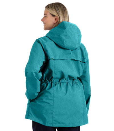 Plus size woman, back view, wearing a JunoActive plus size wind and rain jacket in malechite blue. The jacket has a cinched waist, hood, double front closure and side pockets. The length of the plus size jacket hits just below the hips.