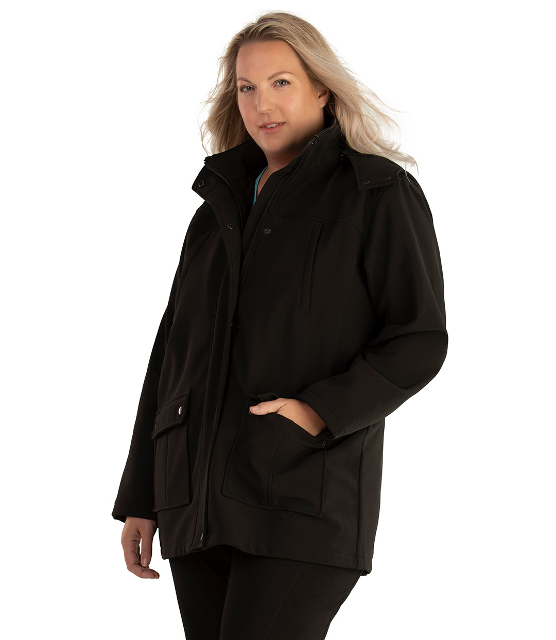 Plus size woman, front side view facing left, wearing a JunoActive plus size Hooded Softshell Jacket in Black. The jacket has a removeable hood, zip front closure, zip chest pocket, and snap patch pockets at the hip. The length of the plus size jacket hits below the hips.