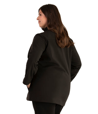 Plus size woman, back side view facing left, wearing a JunoActive plus size Mock Neck Softshell Jacket in Black. The jacket has a mock neck collar, zip front closure, and side pockets. The length of the plus size jacket hits just below the hips.