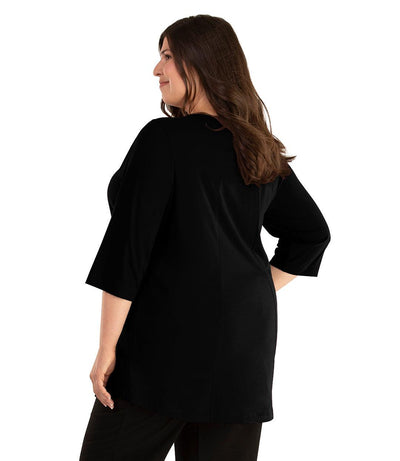 Plus size woman, facing back looking left, wearing JunoActive plus size Stretch Naturals Lite ¾ Sleeve Swing Top in the color Black. She is wearing JunoActive Plus Size Leggings in the color Black.