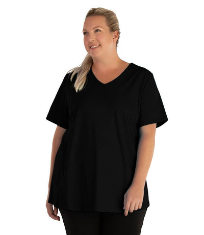 Plus size woman, facing front and looking left, wearing JunoActive plus size Stretch Naturals Lite V-Neck Princess Top in the color Black. She is wearing JunoActive Plus Size Leggings in the color black. 