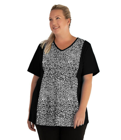 Plus size woman, facing front and looking left, wearing JunoActive plus size Stretch Naturals Lite V-Neck Princess Top in the color Wild Print. She is wearing JunoActive Plus Size Leggings in the color black. 