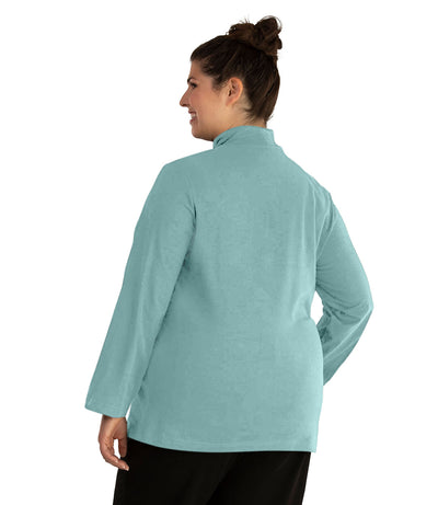Plus size woman, facing back, wearing JunoActive plus size Stretch Naturals Lite Mock Neck Top in the color Robin Blue. She is wearing JunoActive Plus Size Leggings in the color Black.