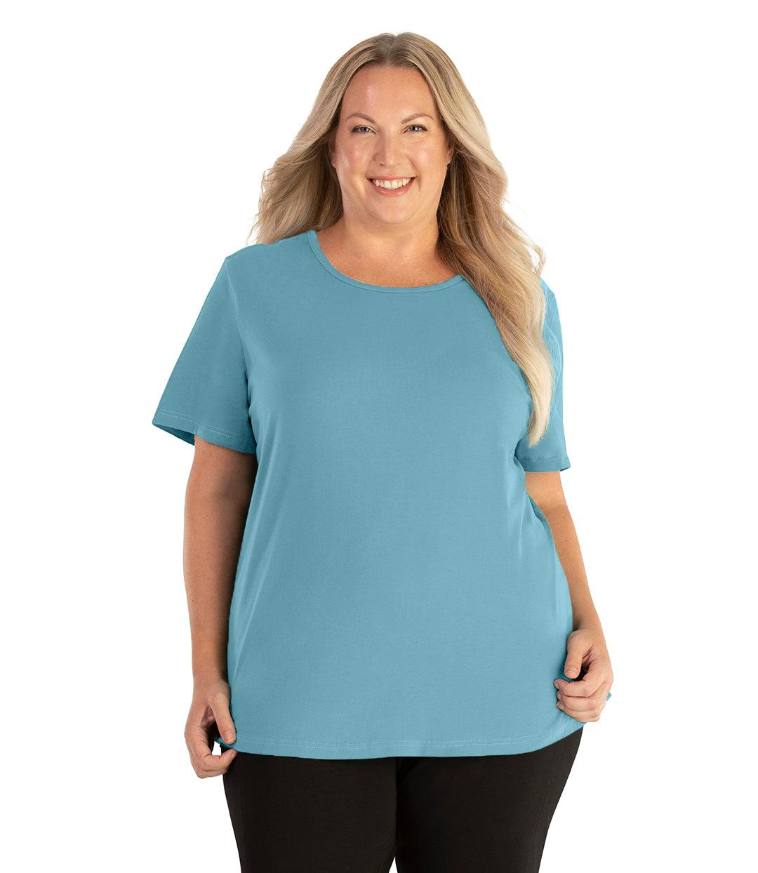 Plus size woman, facing front, wearing JunoActive plus size Stretch Naturals Lite Short Sleeve Scoop Neck Top in the color Mountain Lake Blue. She is wearing JunoActive Plus Size Leggings in the color black. 