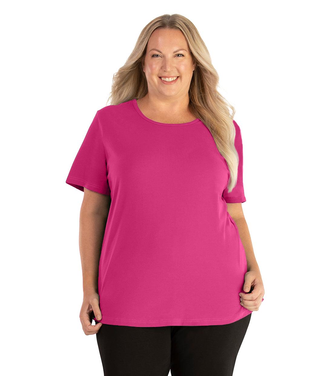 Plus size woman, facing front, wearing JunoActive plus size Stretch Naturals Lite Short Sleeve Scoop Neck Top in the color Poppy Pink. She is wearing JunoActive Plus Size Leggings in the color black. 