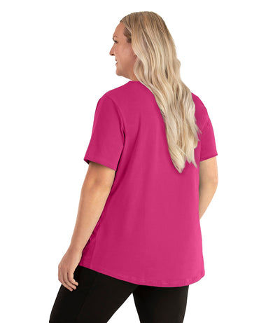 Plus size woman, facing back left, wearing JunoActive plus size Stretch Naturals Lite Short Sleeve Scoop Neck Top in the color Poppy Pink. She is wearing JunoActive Plus Size Leggings in the color black