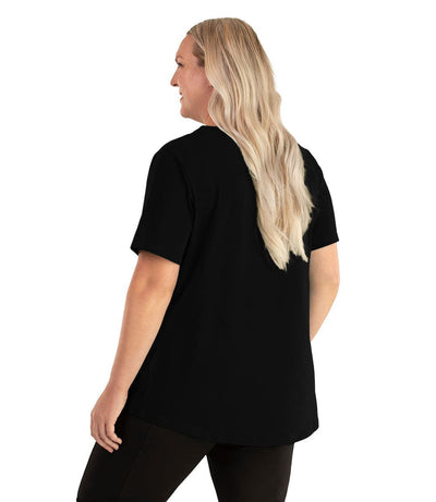 Plus size woman, facing back left, wearing JunoActive plus size Stretch Naturals Lite Short Sleeve Scoop Neck Top in the color Black. She is wearing JunoActive Plus Size Leggings in the color black. 