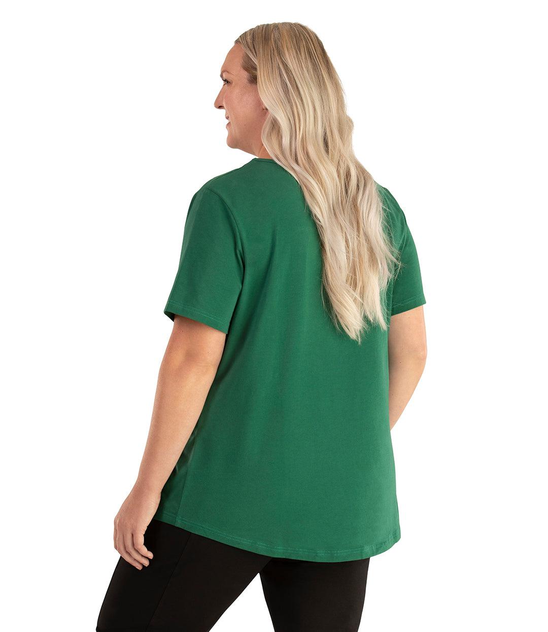 Plus size woman, facing back left, wearing JunoActive plus size Stretch Naturals Lite Short Sleeve Scoop Neck Top in the color Forest Green. She is wearing JunoActive Plus Size Leggings in the color black. 