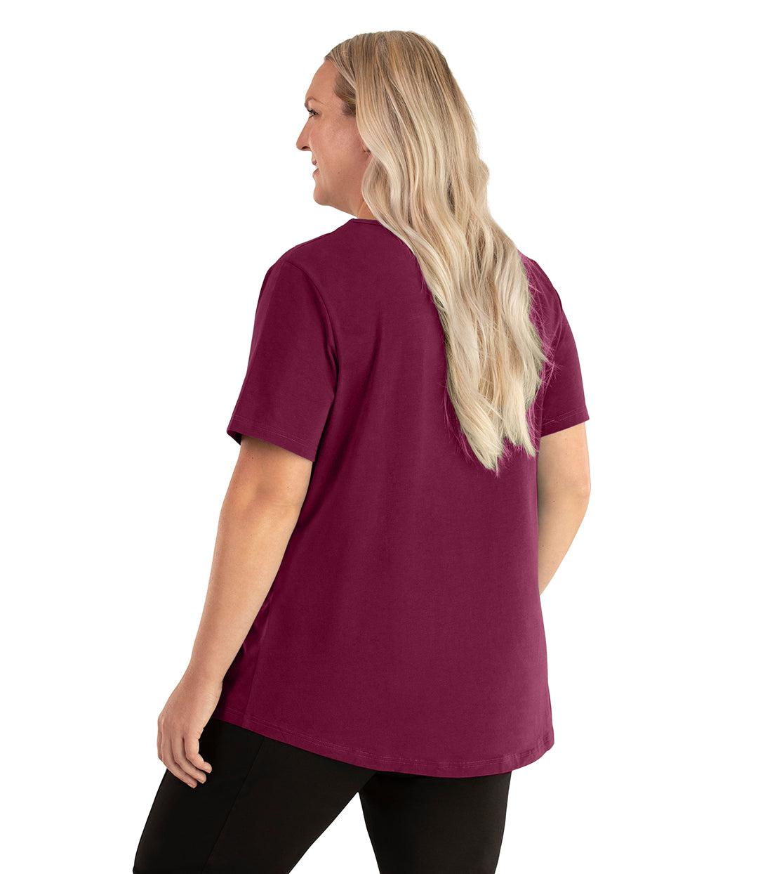 Plus size woman, facing back left, wearing JunoActive plus size Stretch Naturals Lite Short Sleeve Scoop Neck Top in the color Magenta. She is wearing JunoActive Plus Size Leggings in the color black. 