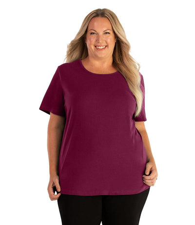 Plus size woman, facing front, wearing JunoActive plus size Stretch Naturals Lite Short Sleeve Scoop Neck Top in the color Magenta. She is wearing JunoActive Plus Size Leggings in the color black. 