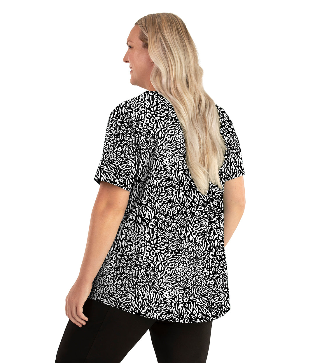 Plus size woman, facing back left, wearing JunoActive plus size Stretch Naturals Lite Short Sleeve Scoop Neck Top in the color Wild Print. She is wearing JunoActive Plus Size Leggings in the color black.