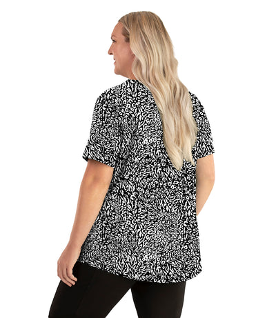 Plus size woman, facing back left, wearing JunoActive plus size Stretch Naturals Lite Short Sleeve Scoop Neck Top in the color Wild Print. She is wearing JunoActive Plus Size Leggings in the color black.