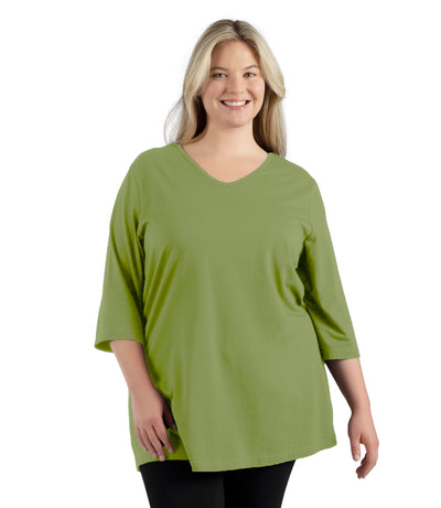 Plus size woman, facing front, wearing JunoActive’s Stretch Naturals Lite 3/4 Sleeve V-neck Tunic, color aloe green. Arms by side.