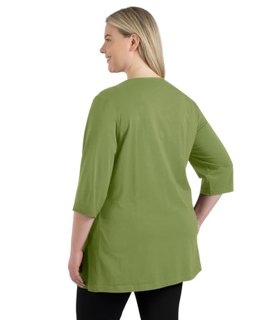 Plus size woman, facing back, wearing JunoActive’s Stretch Naturals Lite 3/4 Sleeve V-neck Tunic, color aloe green.