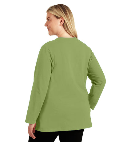 Plus size woman, facing back, wearing JunoActive’s Stretch Naturals Lite Long sleeve scoop neck top, in color aloe green, with her hands by her side. Leggings in black. 
