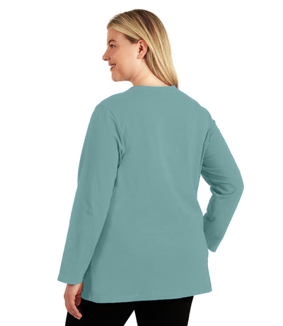 Plus size woman, facing back, wearing JunoActive’s Stretch Naturals Lite Long sleeve scoop neck top, in color robin blue, with her hands by her side. Leggings in black. 