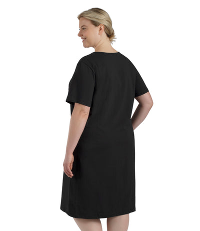 Plus size woman, facing back, wearing JunoActive plus size JunoBliss Sleep Dress in color black. The hem falls just below her knee.