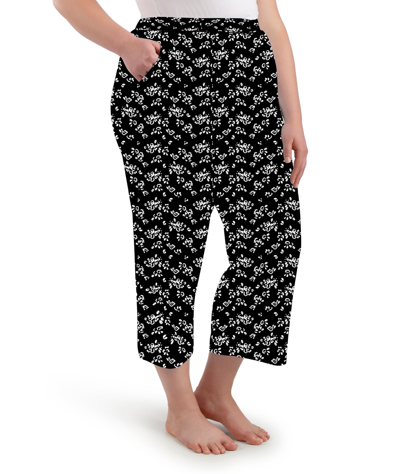 Plus size woman wearing JunoActive's JunoBliss pocketed sleep capris in fresh gardenia print facing the side with right hand in pant pocket.