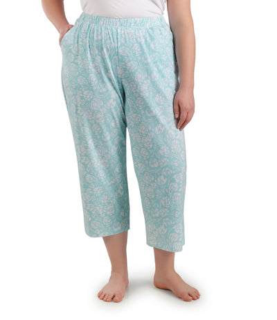Bottom half of plus sized woman, facing front, wearing JunoActive JunoBliss Pocketed Sleep Capris Spring Blue Floral Print. The capri hemline is a few inches above ankle and a little longer than mid calf. Pockets on both sides.