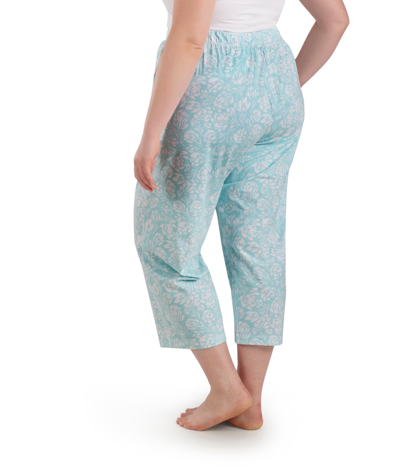 Bottom half of plus sized woman, facing back, wearing JunoActive JunoBliss Pocketed Sleep Capris Spring Blue Floral Print. The capri hemline is a few inches above ankle and a little longer than mid calf. Pockets on both sides.