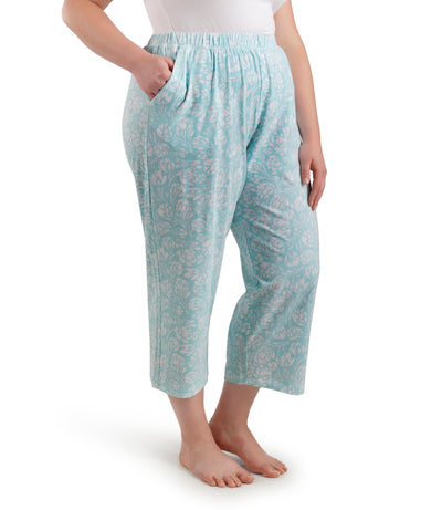 Bottom half of plus sized woman, facing front and angled to the side, wearing JunoActive JunoBliss Pocketed Sleep Capris Spring Blue Floral Print. The capri hemline is a few inches above ankle and a little longer than mid calf. Pockets on both sides.