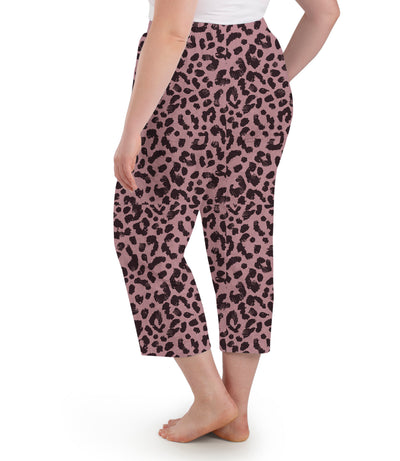 Plus size woman, facing back, wearing JunoActive’s JunoBliss Pocketed Sleep capri in jungle rose print. One hand in pocket and other by her side.