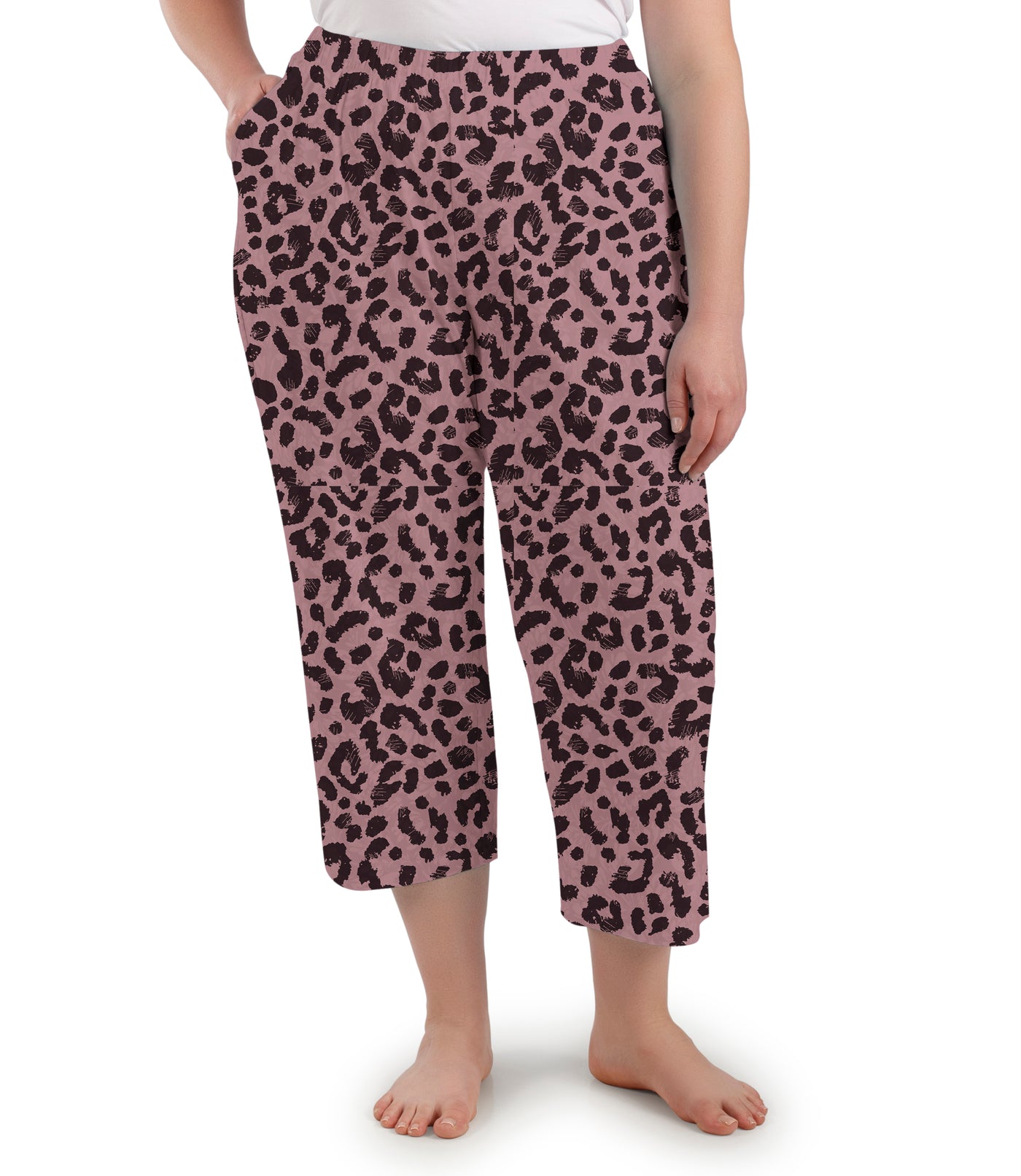 Plus size woman, facing front, wearing JunoActive’s JunoBliss Pocketed Sleep capri in jungle rose print. One hand in pocket and other by her side.