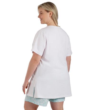 Plus size woman, facing back, wearing JunoBliss V-Neck Short Sleeve Top in color white. Hands down by sides. Side hem split showing.