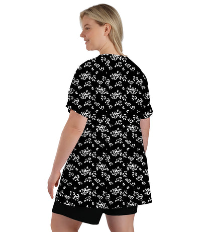 Plus size model, facing back, wearing JunoActive's JunoBliss v-neck short sleeve top in fresh gardenia with black shorts. Hands by her side.