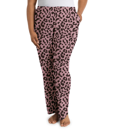 Plus size woman, facing front, wearing JunoActive’s JunoBliss Pocketed Sleep pant in color jungle rose print. One hand in pocket and other by her side.
