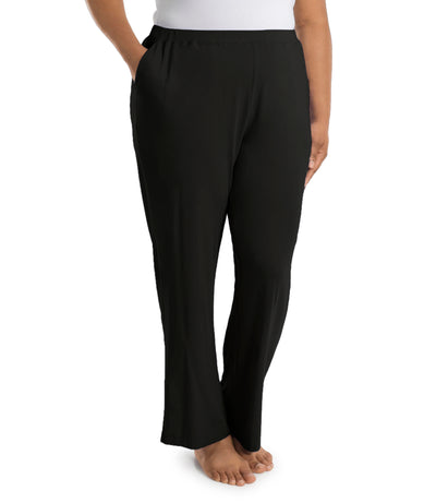 Plus size woman, facing side, wearing JunoActive’s JunoBliss Pocketed Sleep pant in color black. One hand in pocket and other by her side. 