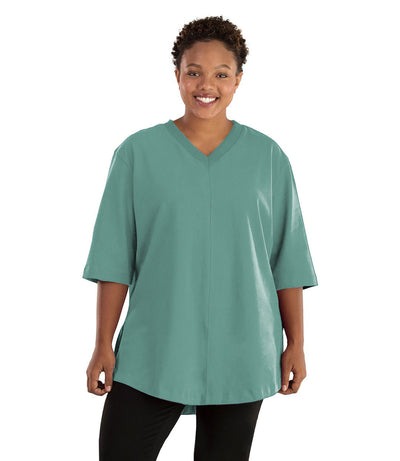 Plus size woman, facing front, wearing JunoActive plus size Legacy Cotton Casual Tunic in the color Lichen Green. She is wearing JunoActive Plus Size Leggings in the color black.