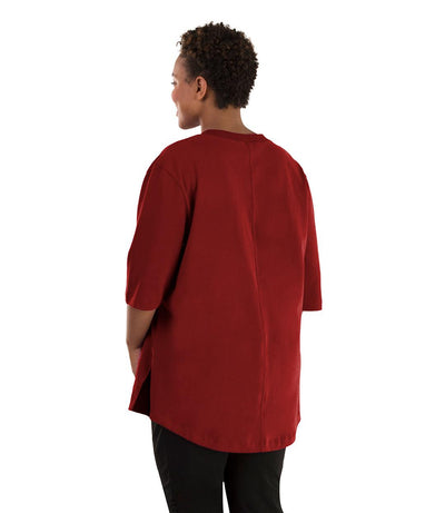 Plus size woman, facing back left, wearing JunoActive plus size Legacy Cotton Casual Tunic in the color Merlot Red. She is wearing JunoActive Plus Size Leggings in the color black.