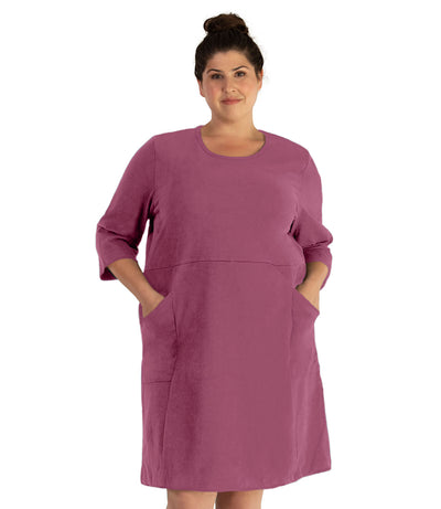 Plus size woman, facing front, wearing JunoActive plus size Legacy Cotton Casual ¾ Sleeve Dress in the color Dusty Rose. Both hands are in the dress pockets at her hip. The dress length is at her knee. 