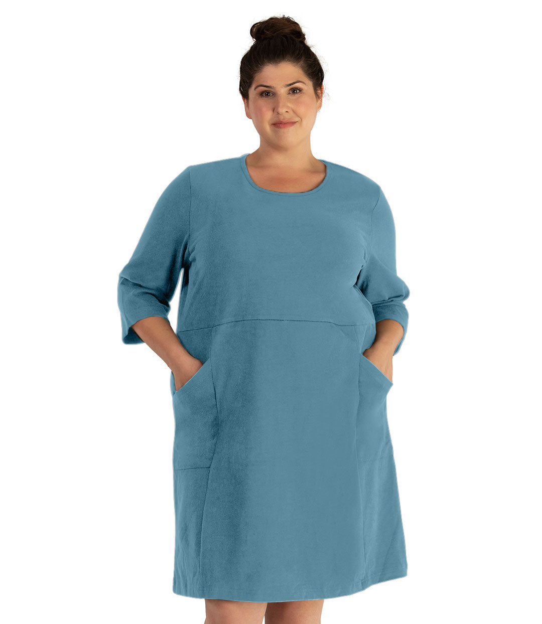 Plus size woman, facing front, wearing JunoActive plus size Legacy Cotton Casual ¾ Sleeve Dress in the color Arctic Blue. Both hands are in the dress pockets at her hip. The dress length is at her knee. 