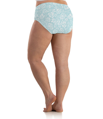 Bottom half of plus sized woman, back view, wearing JunoActive Junowear Cotton Stretch Classic Brief in spring blue floral print. This brief fits to the waistline with conservative leg opening. Print has white flowers on a light blue green background.
