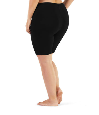 Bottom half of plus sized woman, back view, wearing JunoActive Stretch Naturals Bike Shorts in color black. Bottom hem is a few inches above the knee.